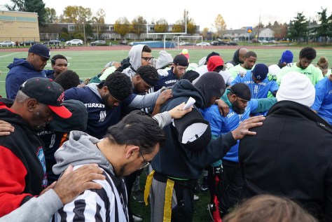 Photo depicting youth football players gathered in prayer before a game on a football field.