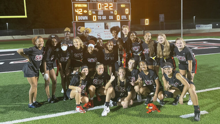 The Sparkman High School girls flag football team standing in front of a score board