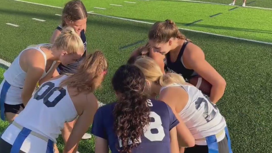 Girls on the Alonso and Robinson High Schools flag football team huddle on the field. 